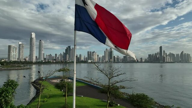 Aerial video of skyscrapers and a flag on the sea shore on a cloudy day