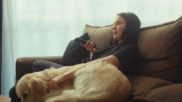 Girl with tv remote control lazily playing with her golden retriever on the couch