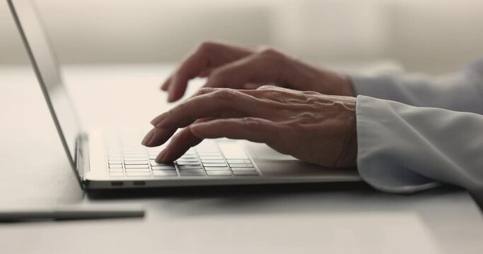 Hands and fingers of professional woman pressing buttons on keyboard, typing on laptop computer placed on work office table, using modern technology, digital gadget for business. Close up cropped shot