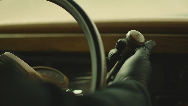 Close up view of male hand with black gloves, rotating or turning car key or gear shifting inside classic vintage suv car with beige colored interior : Concept of  robbery or thief . Jeep Wagoneer