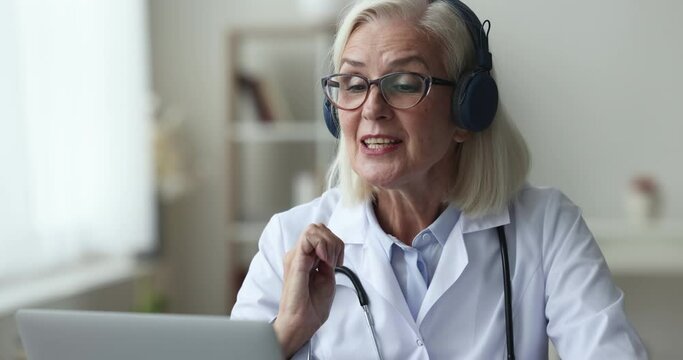 Positive caring doctor in headphones talking to patient on video call, giving consultation, recommendation about treatment, online support, speaking at laptop computer, smiling