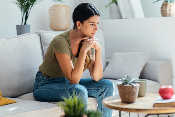 Worried sad woman thinking while sitting on couch in the living room at home
