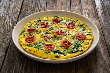 Delicious breakfast - scrambled eggs with spinach and cherry tomatoes on wooden table