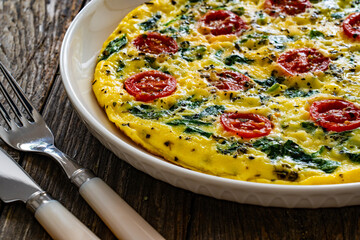 Delicious breakfast - scrambled eggs with spinach and cherry tomatoes on wooden table