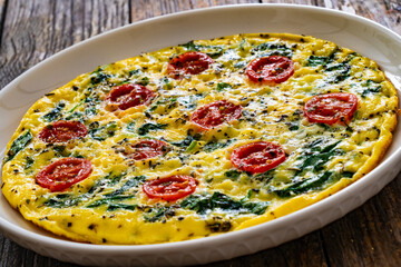 Delicious breakfast - scrambled eggs with spinach and cherry tomatoes on wooden table