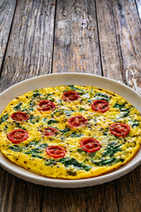Delicious breakfast - scrambled eggs with spinach and cherry tomatoes on wooden table