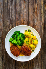 Seared pork meatballs with boiled potatoes and  broccoli  on wooden table
