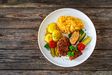 Seared pork meatballs with boiled potatoes and sauerkraut on wooden table

