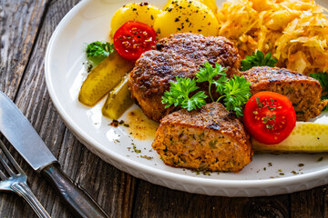 Seared pork meatballs with boiled potatoes and sauerkraut on wooden table
