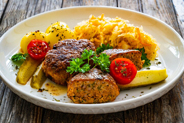 Seared pork meatballs with boiled potatoes and sauerkraut on wooden table
