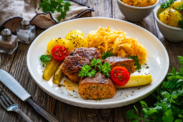 Seared pork meatballs with boiled potatoes and sauerkraut on wooden table
