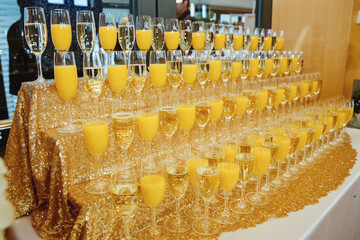 A lot of wine glasses with champagne and orange juice on the table at the ceremony. Selective focus.