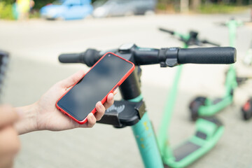 Woman rents electric scooter using mobile phone app at the street. Renewable energy transport.