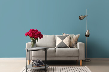 Vase of red peonies with coffee table, couch and floor lamp near blue wall