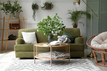 Interior of light living room with green sofa and blooming jasmine flowers on coffee table