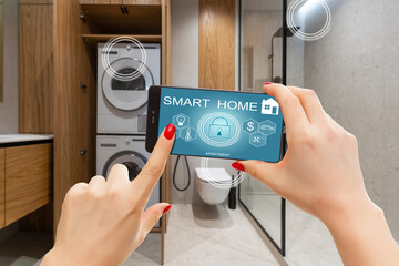 Smart home technology interface on smartphone app screen with augmented reality (AR) view of internet of things (IOT) connected objects in the apartment interior, person holding device.