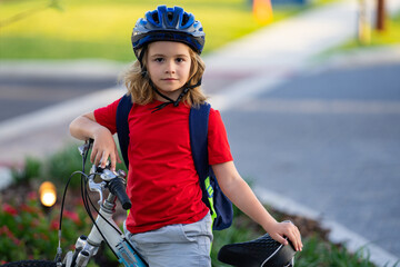 Naklejka premium Child on bicycle. Boy in a helmet riding bike. Little cute caucasian boy in safety helmet riding bike in city park. Child first bike. Kid outdoors summer activities. Kid on bicycle. Boy ride a bike.