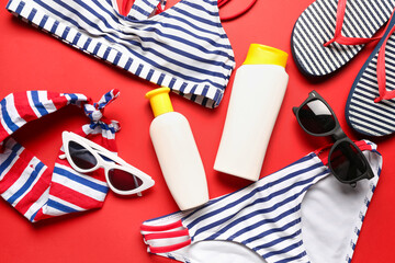 Sunglasses with swimsuit, flip flops and bottles of sunscreen cream on red background