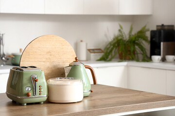 Toaster, electric kettle, juicer and cutting board on wooden table in modern kitchen