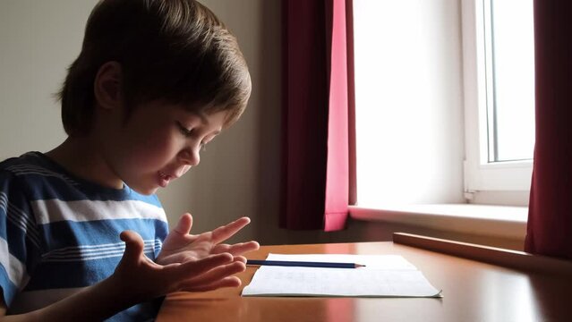 The boy counts on his fingers the mathematics example. The child is sitting at the table and doing a maths homework. Smart kid. School preparation.