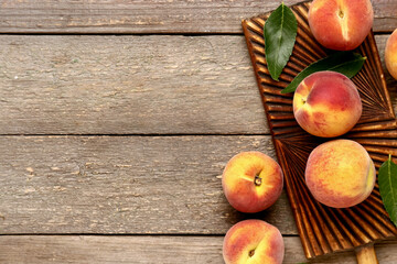 Board with sweet peaches and leaves on wooden background