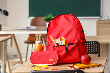 Red school backpack with stationery and lunch on desk in classroom