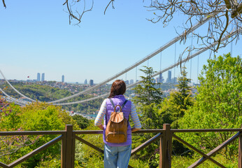 A young woman tourist with a backpack enjoys a panoramic view of the Fatih Sultan Mehmet Bridge. Back view.The photo was taken from Otagtepe