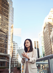 Fototapeta premium Young busy pretty Asian business woman professional office manager executive or global international company employee standing on big city street outside using digital tablet fintech device, vertical.