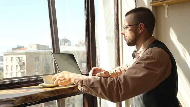 Man with glasses by the window working at a computer on a sunny day