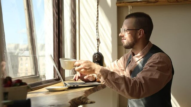 Man with glasses by the window working at a computer on a sunny day