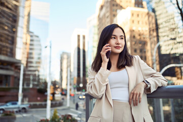 Young pretty Asian business woman office professional holding cellphone in hands standing on big...