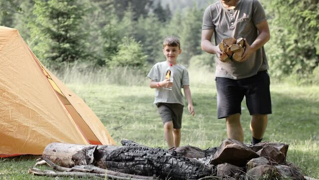 Father and son carry firewood and firestarter for the fire during trip in natural environment.