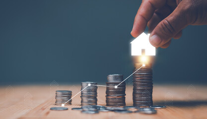 Investment for real estate concept, Businessman's hand putting house icon on top of coins stack and...