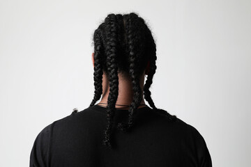 Back view shot of dark-skinned young man with afro braids posing in the studio.