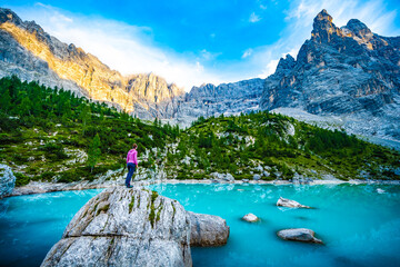 Athletic woman enjoys beautiful view from huge boulder  on turquoise Sorapis lake with dito di dio...