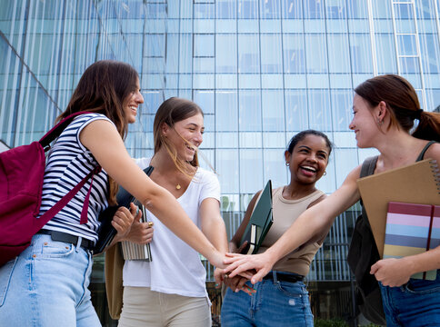 Group of four multi-ethnic student girls shake hands on a campus . Empowered women, feminism , student girls