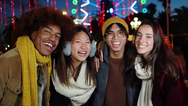 Group of multiethnic friends having fun in a city street during a winter night illuminated at Christmas