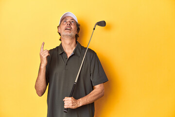 Middle-aged golfer with club and cap on yellow pointing upside with opened mouth.