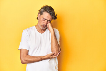 Middle-aged man posing on a yellow backdrop who feels sad and pensive, looking at copy space.