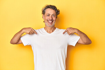 Middle-aged man posing on a yellow backdrop surprised pointing with finger, smiling broadly.