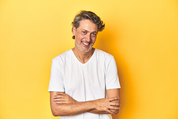 Middle-aged man posing on a yellow backdrop laughing and having fun.