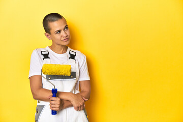 Young female painter with yellow paint roller, studio backdrop