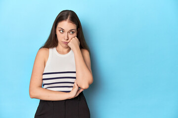 Woman in a striped top posing on a blue studio backdrop who feels sad and pensive, looking at copy space.
