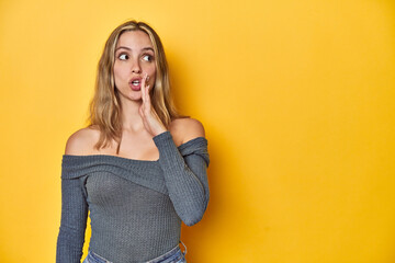 Elegant blonde on yellow backdrop, is saying a secret hot braking news and looking aside