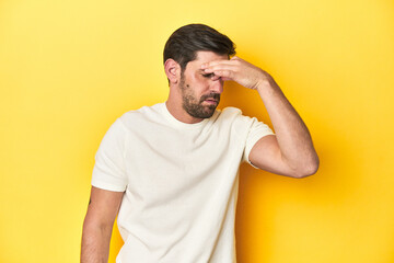 Fototapeta na wymiar Caucasian man in white t-shirt on yellow studio background having a head ache, touching front of the face.