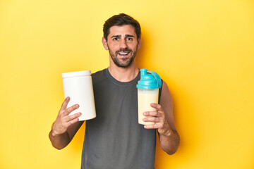 Man in sportswear with protein shake and powder on yellow studio background.