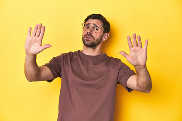 Man making a stop gesture on a yellow studio background. - obrazy, fototapety, plakaty