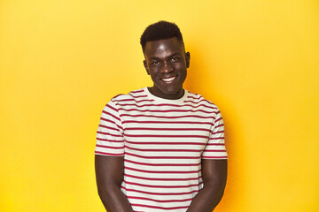 Obraz premium Stylish young African man on vibrant yellow studio background, laughs and closes eyes, feels relaxed and happy.