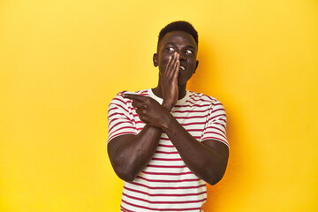 Stylish young African man on vibrant yellow studio background, saying a gossip, pointing to side reporting something.