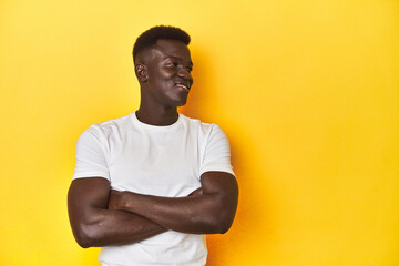 Fototapeta premium Stylish young African man on vibrant yellow studio background, smiling confident with crossed arms.